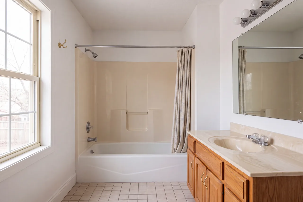 A dated bathroom with a fiberglass tub surround and an oak vanity