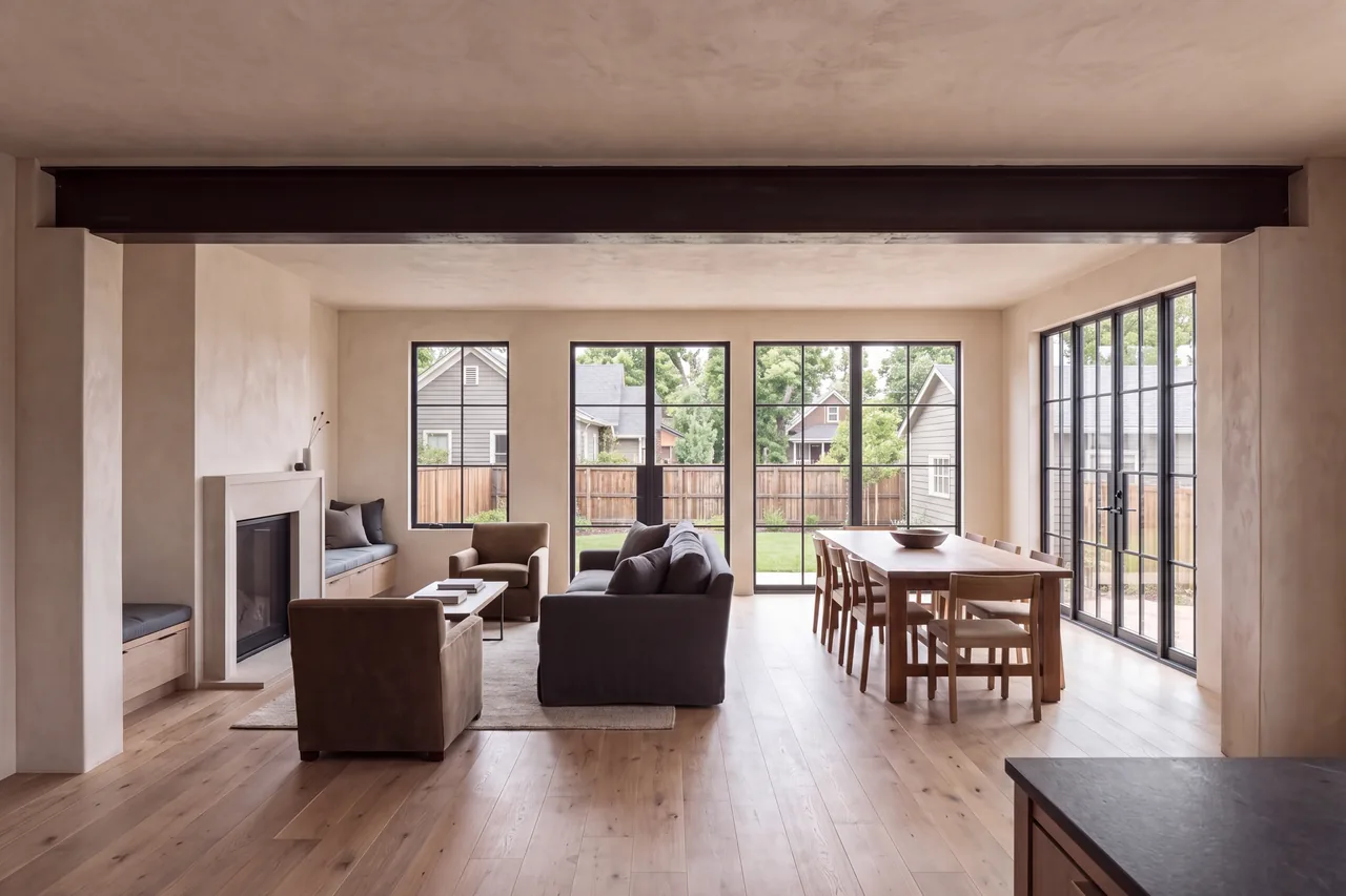 The same space renovated into one open room under a steel beam, with oak floors and a plaster fireplace