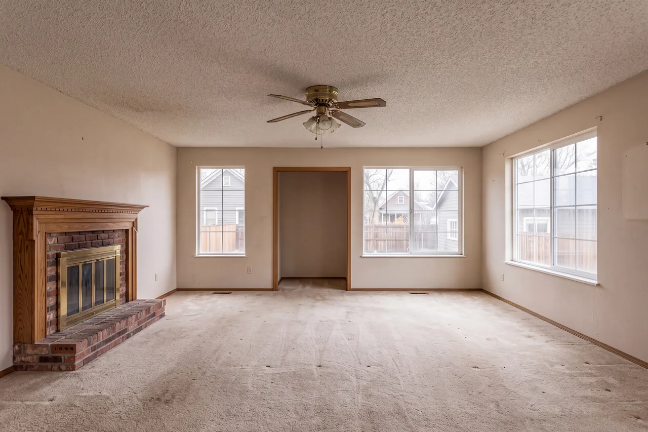 A dated living room closed off from the dining room by a wall, with carpet and a brick fireplace