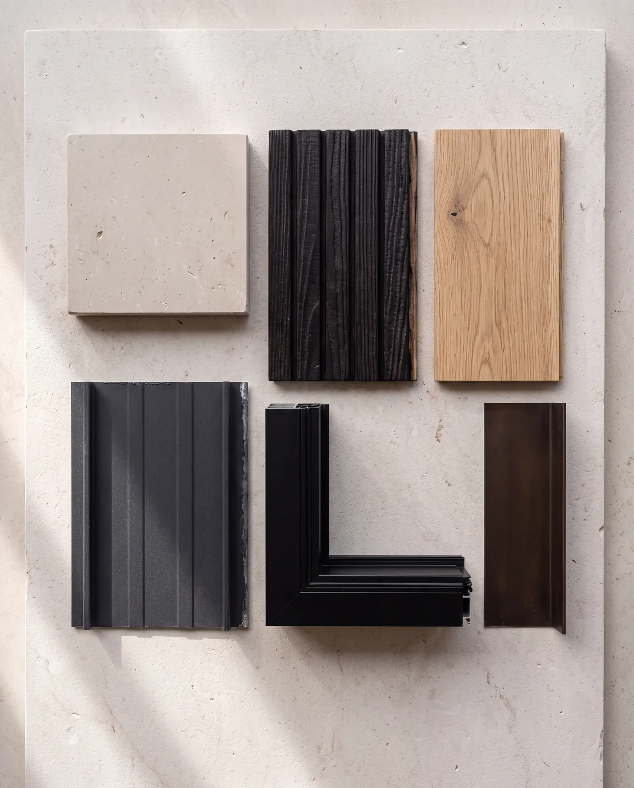 Samples of limestone, charred timber, white oak, metal roofing and a black window frame laid out with even gaps